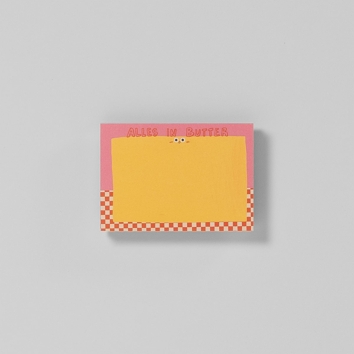 Notizblock A7 „Alles in Butter“ von Illustratorin Slinga – pinker Hintergrund, gelber Butterblock mit Kulleraugen, roter Karo-Rand